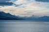 A serene lake with a backdrop of snow-capped mountains under a partly cloudy sky