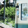 A train conductor wearing a mask and uniform looks out from the door of a train